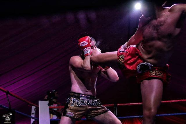 Two muay thai fighters compete in a kickboxing match with intense action and dramatic lighting.