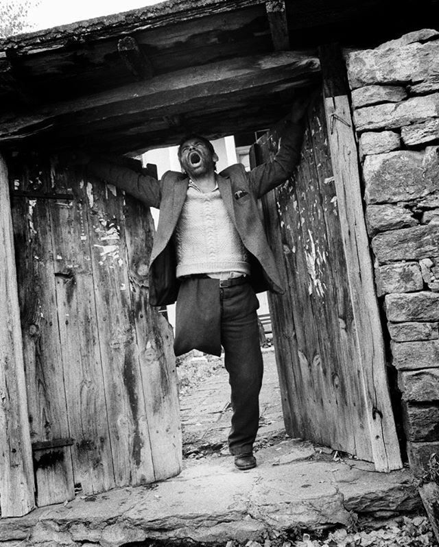 A man stands in a doorway, appearing distressed in this black and white image, conveying struggle and emotional intensity.