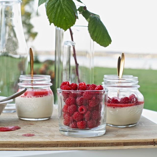 Three jars of raspberries, with one having pudding, are set on a wooden table, perfect for dessert or breakfast.