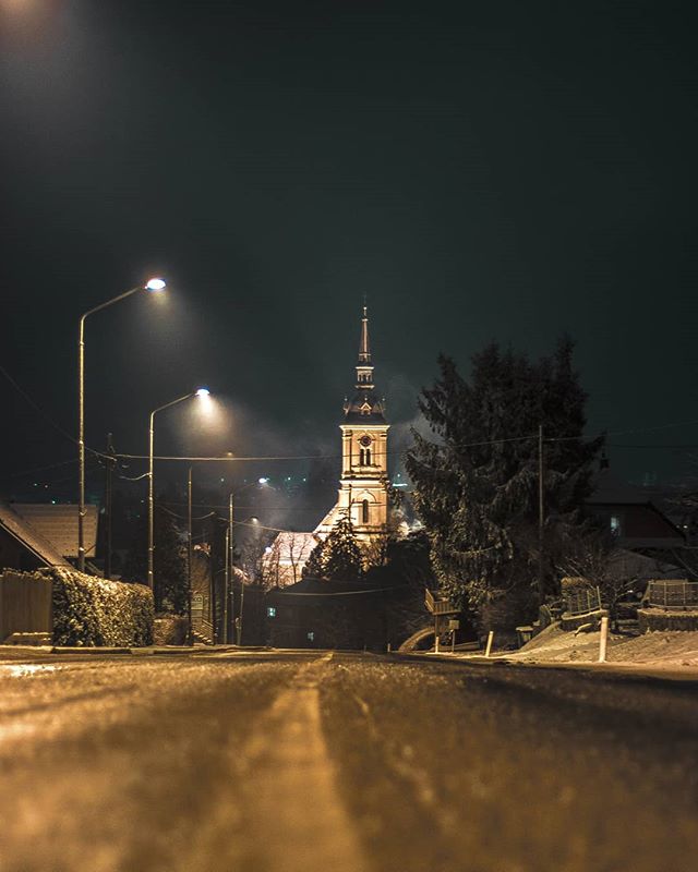 A street view at night with a church illuminated in the background during winter, creating a serene cityscape.