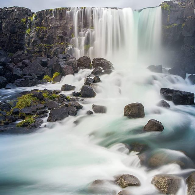 A serene, long-exposure shot of Skogafoss waterfall in Iceland, showcasing blurred water flowing over dark rocks.