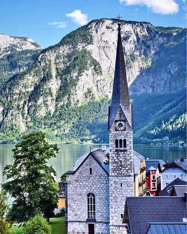 Picturesque Hallstatt church, Austria, nestled by a serene lake with majestic mountains in the background.