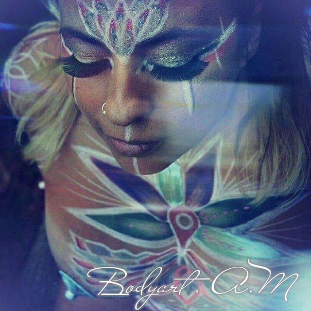 A woman with intricate body art and face paint poses for a close-up shot.