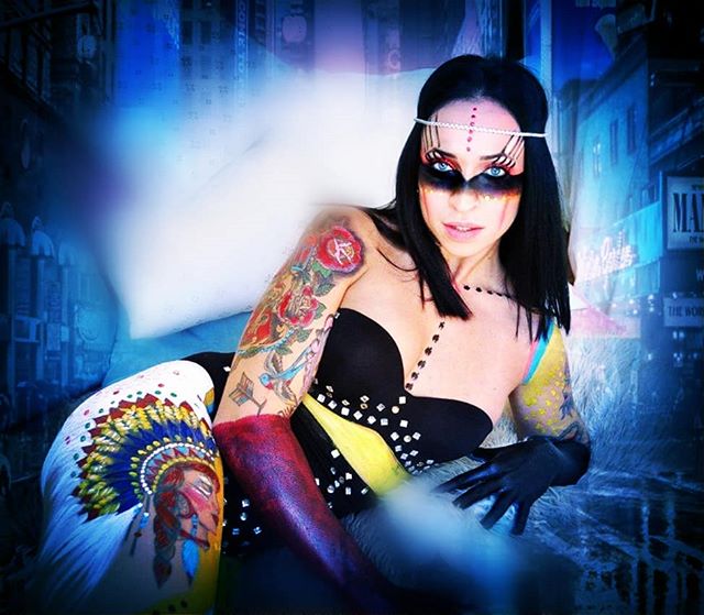 A woman with tattoos and body paint poses dramatically against an urban backdrop for a striking editorial image.