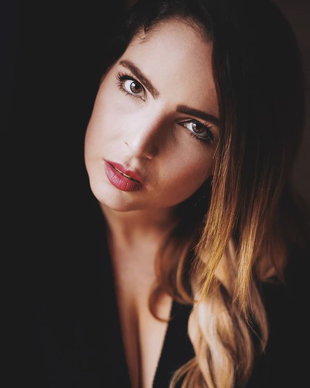 A beautiful brunette woman with red lipstick gazes intently in a close-up portrait with soft lighting.
