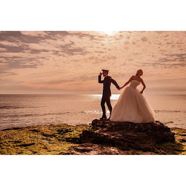 A bride and groom silhouetted against a sunset on a rocky beach during their wedding.