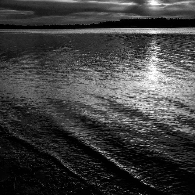 A tranquil, monochromatic scene of a calm lake reflecting soft light under a cloudy sky, perfect for backgrounds and travel themes.