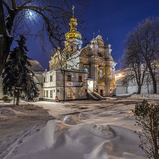 A serene view of a historic church at night, blanketed in snow.
