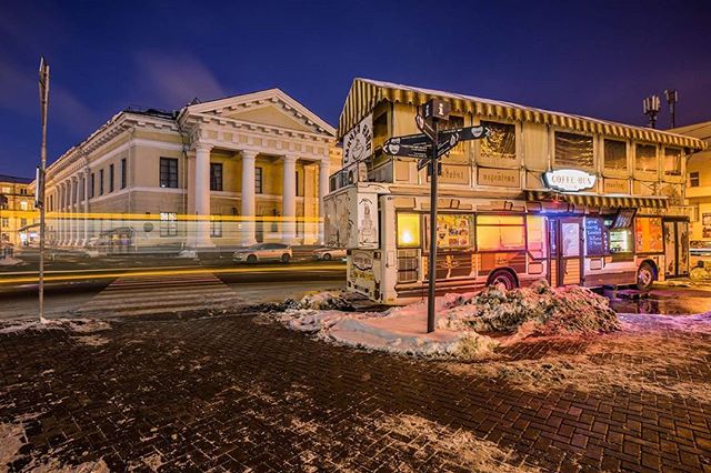 A unique coffee bus stands on a city street with a beautiful building in the background, captured with long exposure.