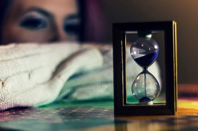 A woman gazes at an hourglass, evoking themes of time, reflection, and patience.