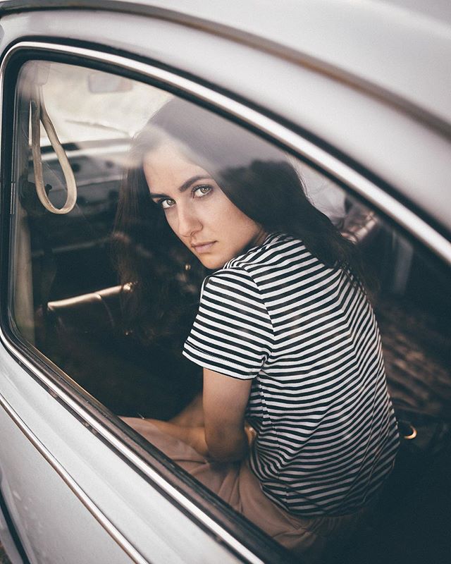 A young woman with dark hair looks back from inside a vintage car.