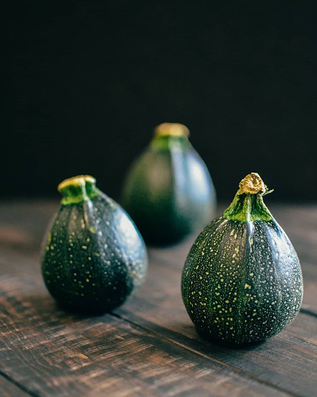 Three fresh zucchini on a rustic wooden table against a dark background. 