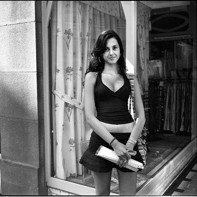 A confident woman stands in front of a storefront in a black and white urban setting.