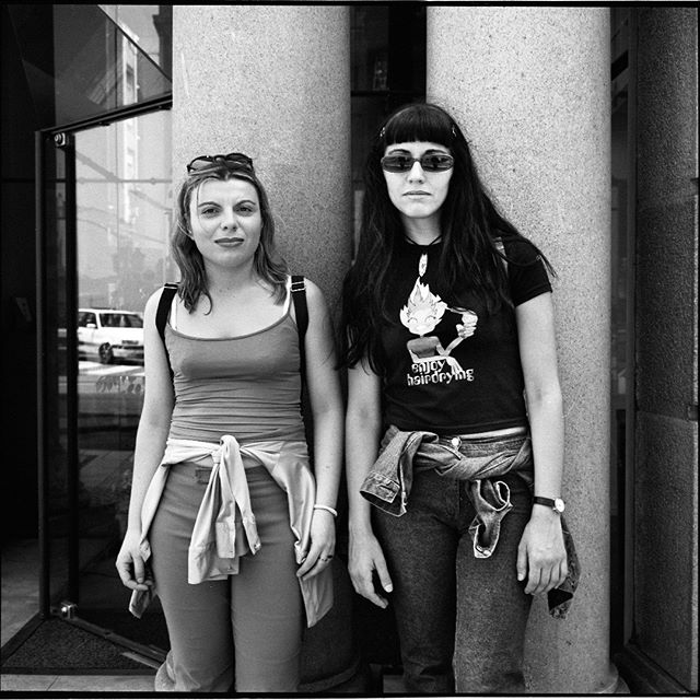 Two women stand in front of a building in an urban setting, showcasing street style and friendship.