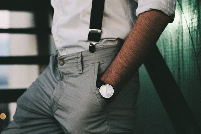 A stylish man with suspenders and a watch stands confidently. Ideal for fashion and lifestyle themes.