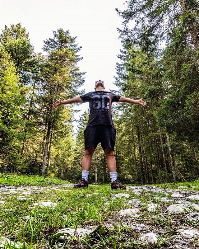 Man standing in a forest with arms outstretched, enjoying nature on a bright day.