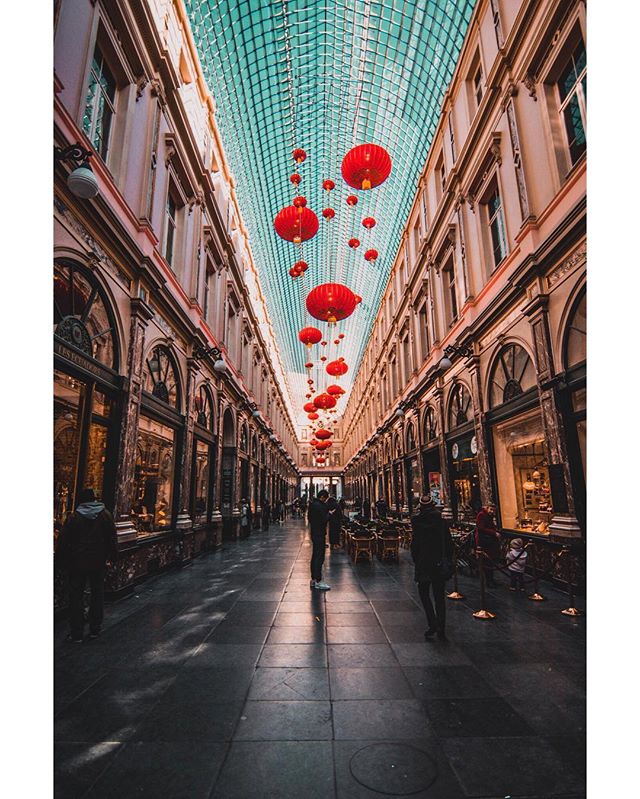 A vibrant indoor shopping arcade with red lanterns and many people strolling through.