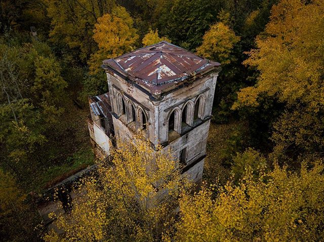 An aerial view shows an old, weathered tower surrounded by autumn trees in a forest.