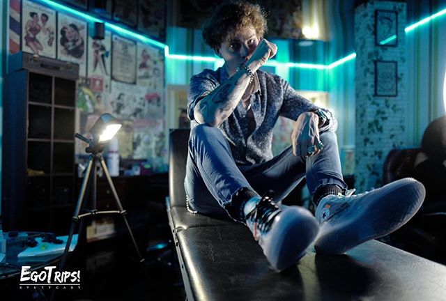 A tattooed man sits in a tattoo parlor, showcasing a relaxed and confident modern style.