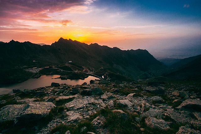 Panoramic mountain landscape with a lake, rocky terrain and a vibrant sunset sky. Ideal for travel and nature themes.