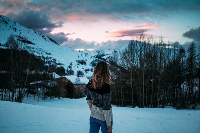 A woman admires the snowy mountains and sunset, a peaceful scene for travel and nature enthusiasts.