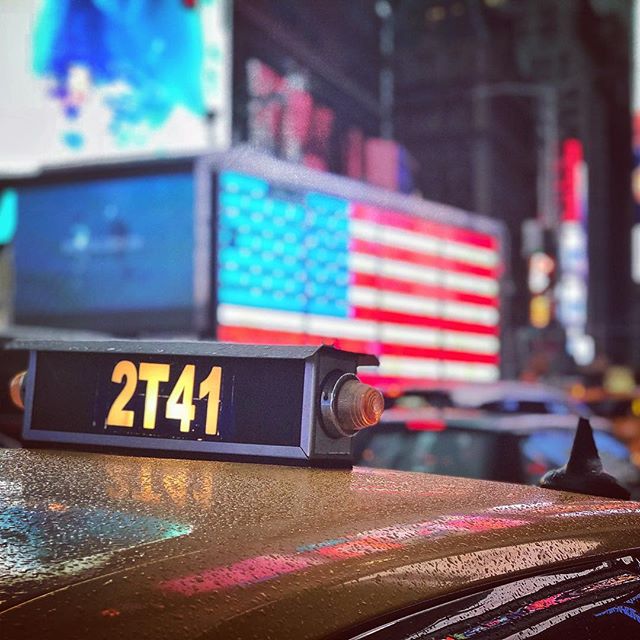 A taxi with sign in Times Square, New York City at night with American flag in the background.