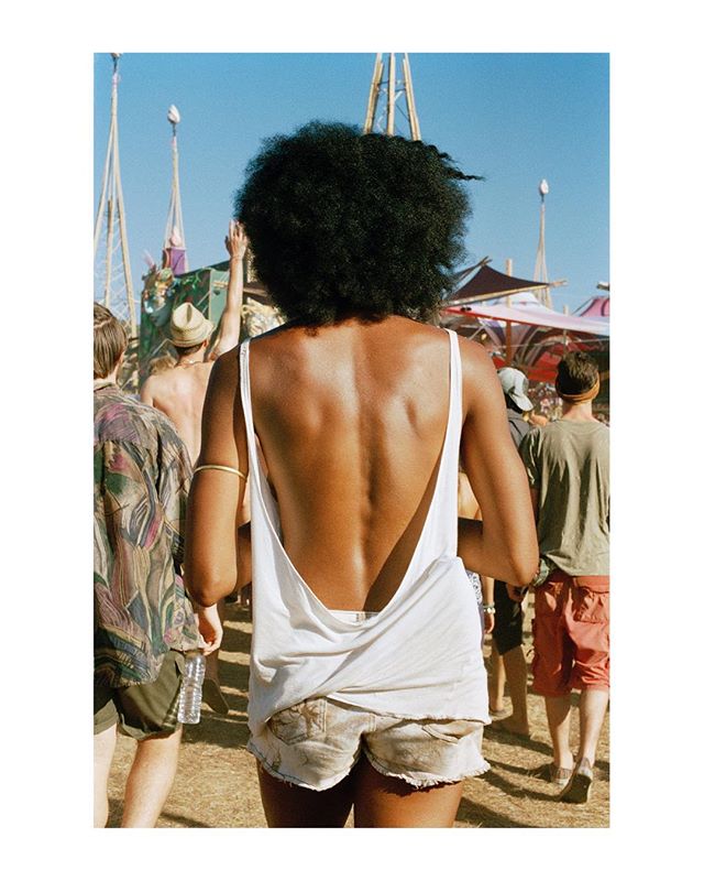 A woman with an afro walks at an outdoor festival with other people during daytime.
