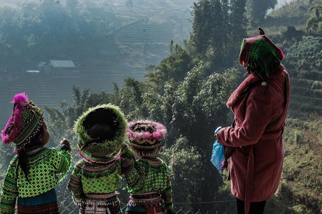 Four people in traditional clothing look out over a mountainous landscape.