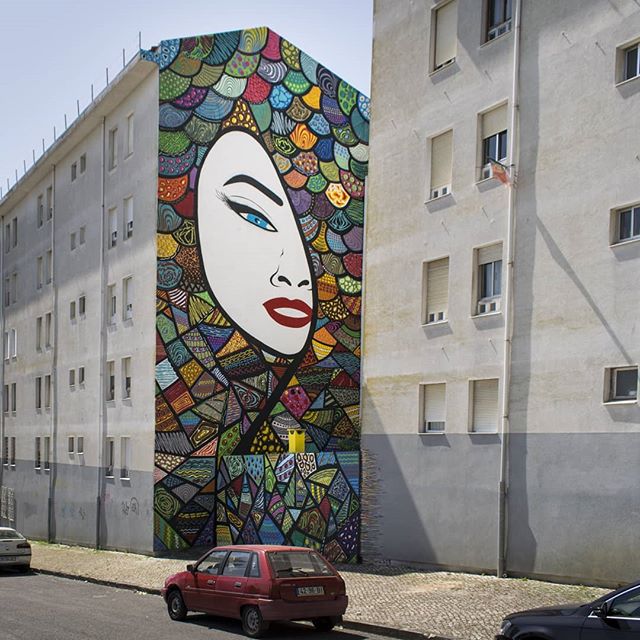 A vibrant mural featuring a woman's face decorates a building in an urban setting, enhancing the cityscape.