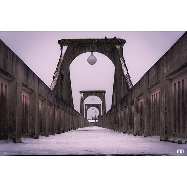 A symmetrical view of a concrete bridge featuring arched entrances and spherical lights during winter.