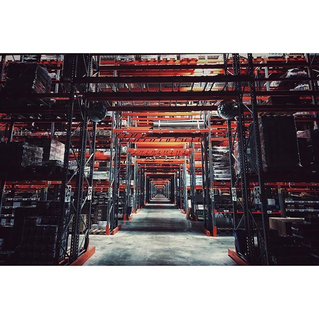 A long aisle stretches into the distance with shelves stacked with products inside a vast warehouse.