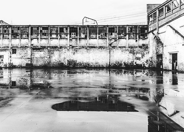 A monochrome shot of an old building reflected in a puddle, capturing an urban landscape with minimalist and vintage style.
