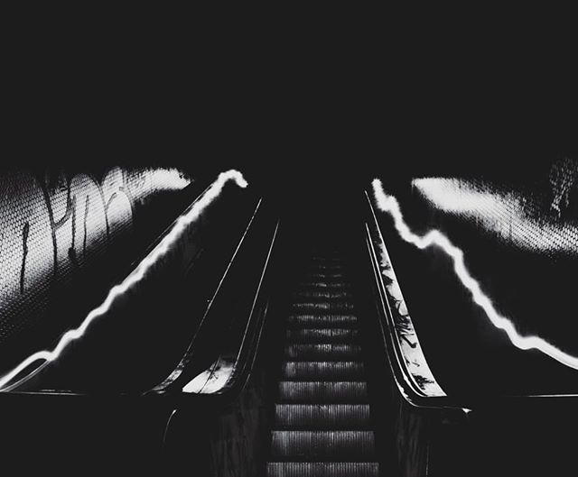 A low-angle shot of an escalator in black and white, shrouded in darkness and mystery.