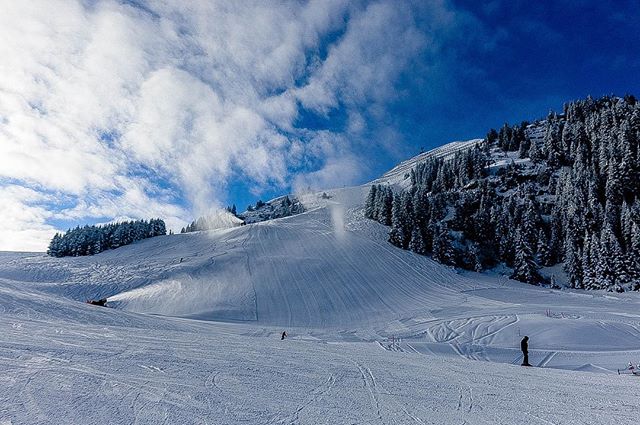 A scenic winter landscape with skiers on a snowy mountain slope under a blue sky with clouds.