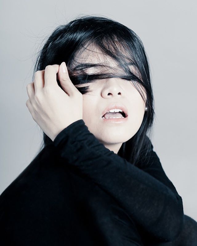 An emotional portrait of a woman with dark hair partially covering her face, captured in a close-up shot.