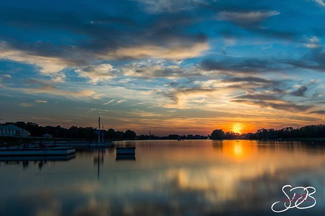 A serene lake reflects a colorful sunset sky, creating a peaceful and inviting scene.