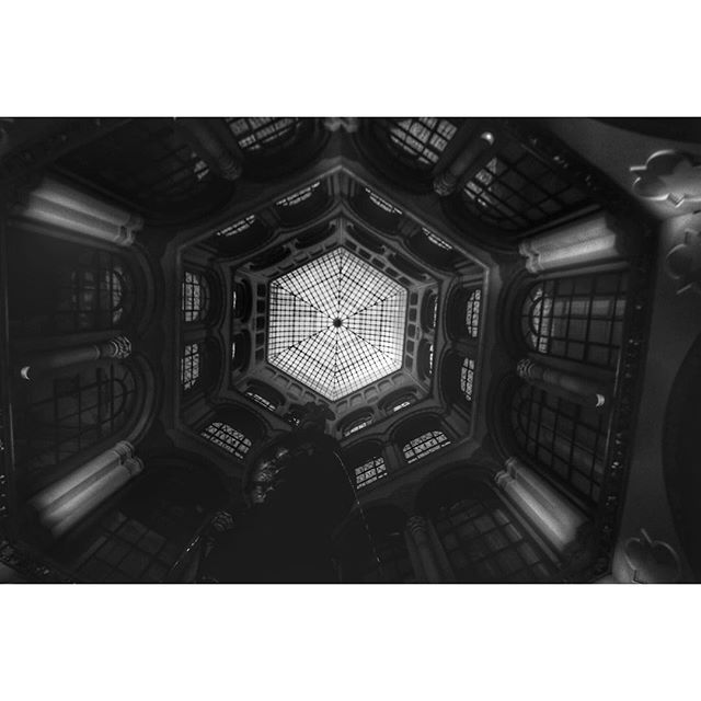 A low angle view of a glass dome ceiling and architectural interior in black and white.