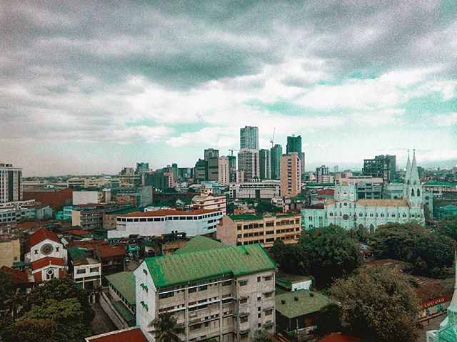 An aerial view captures a cityscape with historic buildings, modern skyscrapers, and cloudy skies in an urban setting.