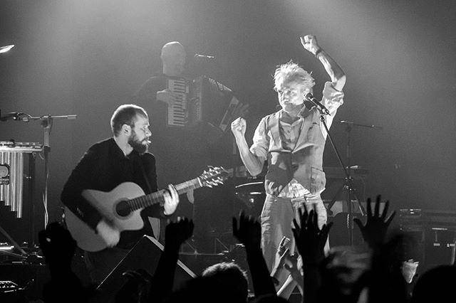 A black and white image of a band performing on stage at a concert in front of a crowd.