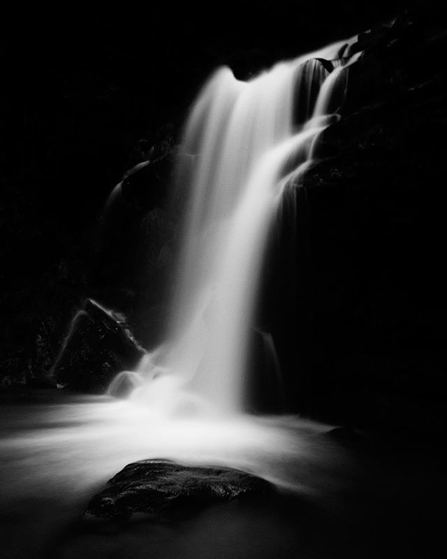 A monochrome, long exposure shot of a cascading waterfall over rocks, creating a sense of serene power and timeless beauty.