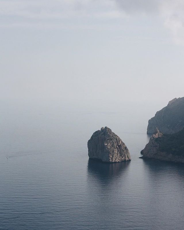 A serene seascape featuring a rocky island and cliffs under a calm, overcast sky.