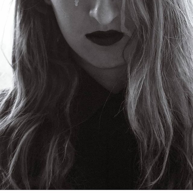 A monochrome close-up portrait of a woman with dark lips and tear, expressing emotion through artistic simplicity.