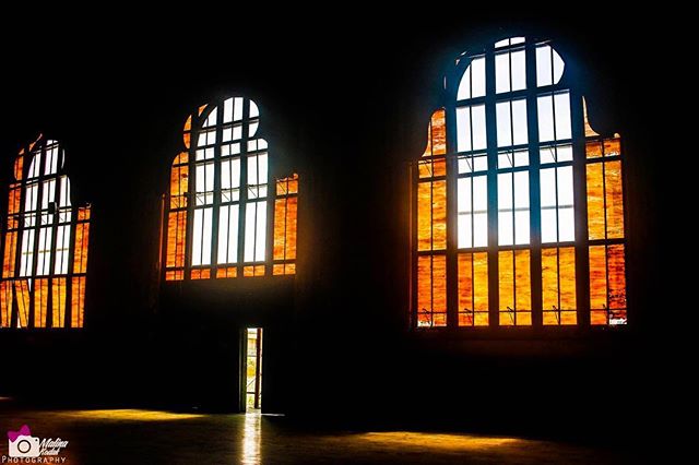 Sunlight streams through the arched windows of a dark interior, creating a striking architectural silhouette.