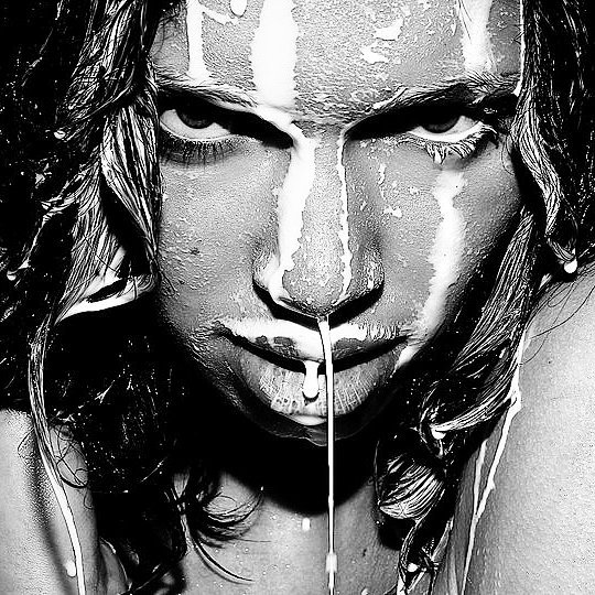 A close-up black and white portrait of a woman's face covered in white liquid, creating a dramatic, artistic effect.