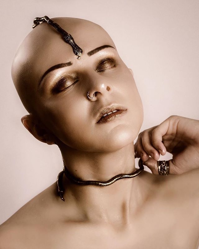 Artistic shot of a bald woman wearing snake jewelry with closed eyes in a studio setting.