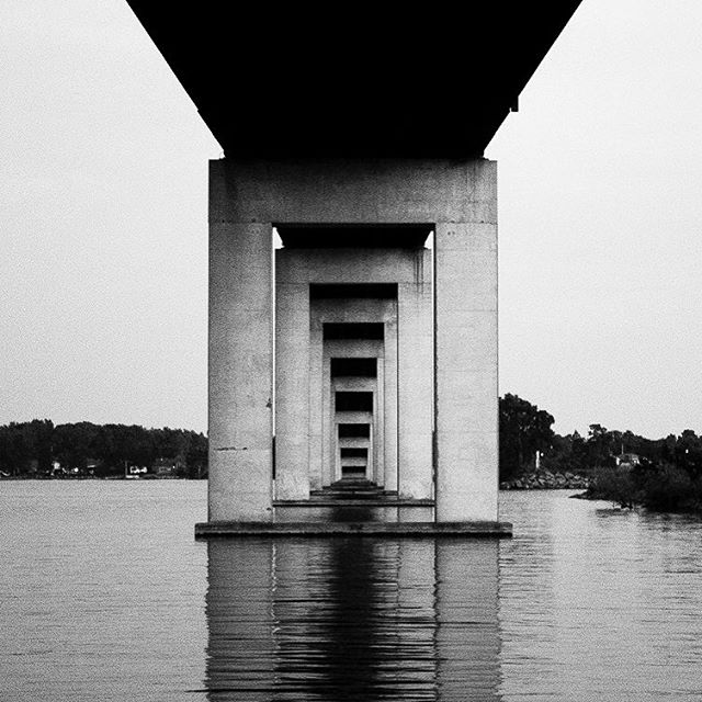 Monochrome shot of a bridge support with water in the background, showcasing architectural design and structural integrity.