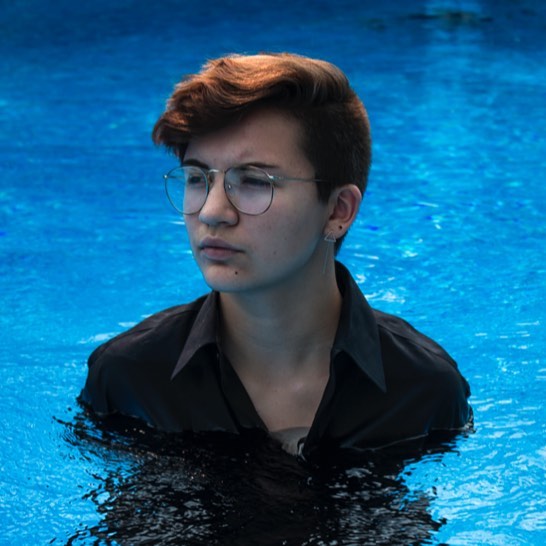 A brunette woman with glasses is in a blue pool, wearing a black shirt.
