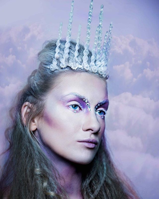A woman with an ice crown and fantasy makeup against a cloud background.