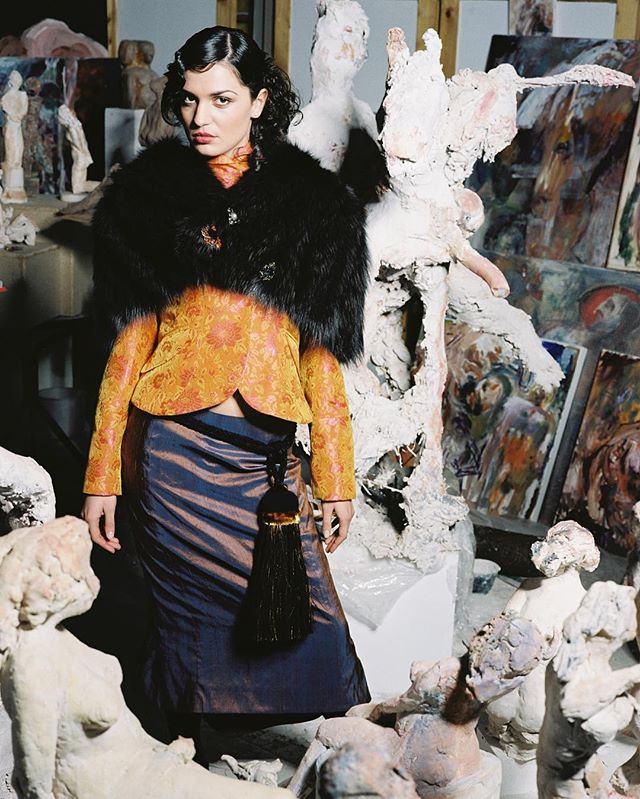 A woman in vintage fashion poses amongst sculptures in an artist's studio for an editorial shot.
