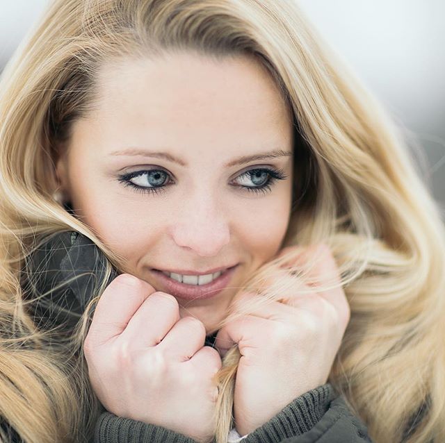 A smiling woman with blonde hair, wearing a winter jacket, poses outdoors in a soft, dreamy atmosphere.
